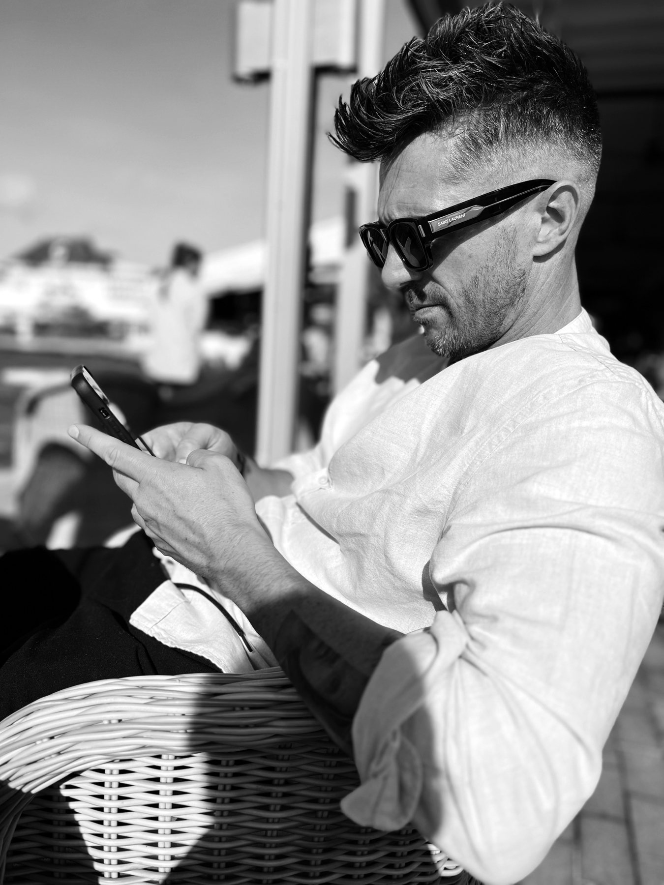 Barry Sutin in zwart-wit, met zonnebril op zijn telefoon kijkend