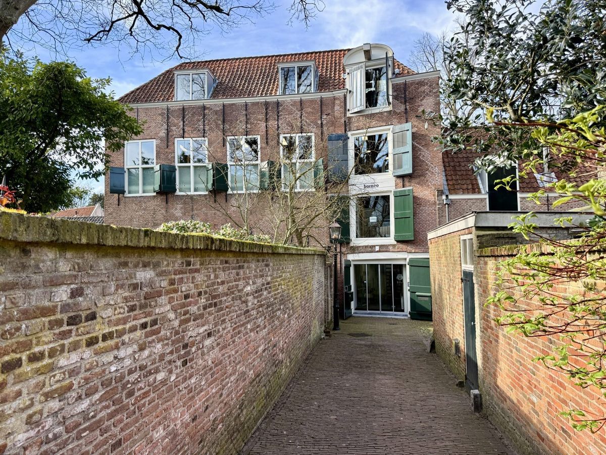 Het monumentale pakhuis aan de Kuiperspoort in Middelburg, met groene luiken en een steegje met bakstenen muren