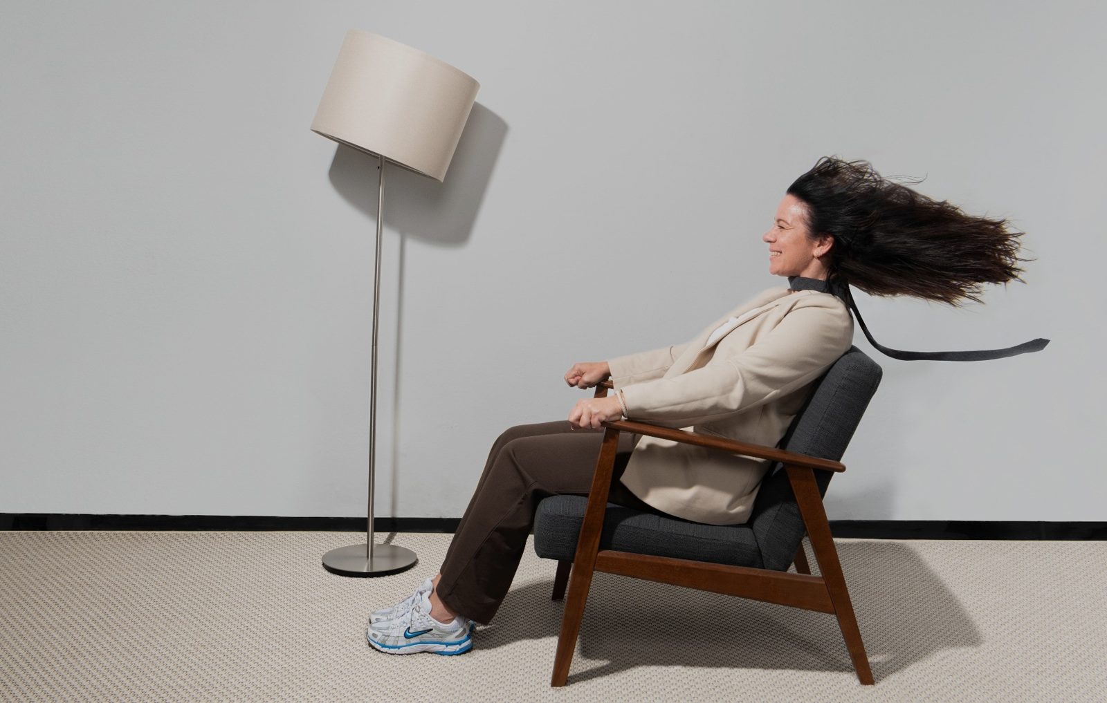 Collega lachend in een fauteuil, haar en stropdas wapperen in de wind